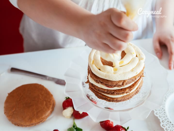 Chef piping vanilla icing onto tiered cake