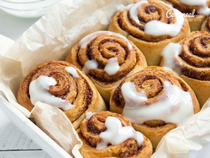 Tray of freshly baked cinnamon rolls drizzled with white icing, served on parchment paper.