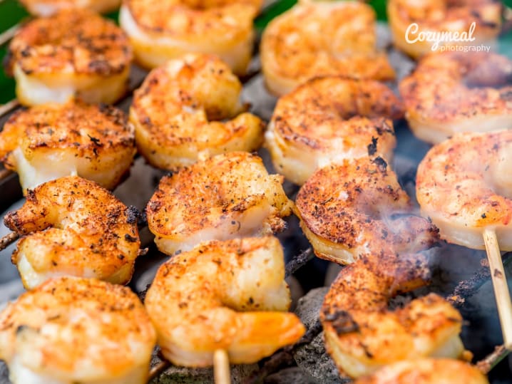 Close up of shrimp skewers cooking on a grill, seasoned with spices and producing smoke