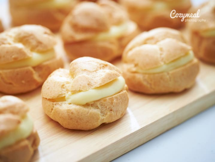 Cream puffs with coffee cream filling â€“ Golden cream puffs filled with coffee cream, arranged neatly on a wooden board.