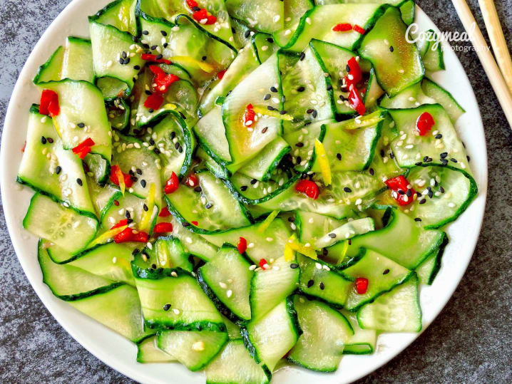 Spicy cucumber salad with red pepper and sesame â€“ A vibrant cucumber salad garnished with red chili slices and sesame seeds, served on a white plate with chopsticks.