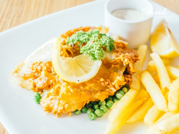 Plated fish and chips with peas and lemon wedge â€“ Crispy beer-battered fish served with golden fries, green peas, and a lemon wedge on a white plate.