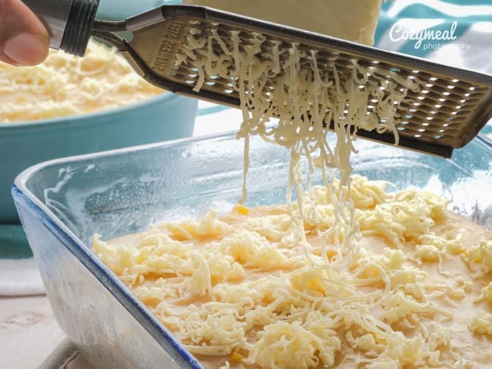 Freshly grated cheese being added to a baking dish of macaroni