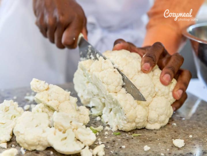 Hands chopping fresh cauliflower on a cutting board