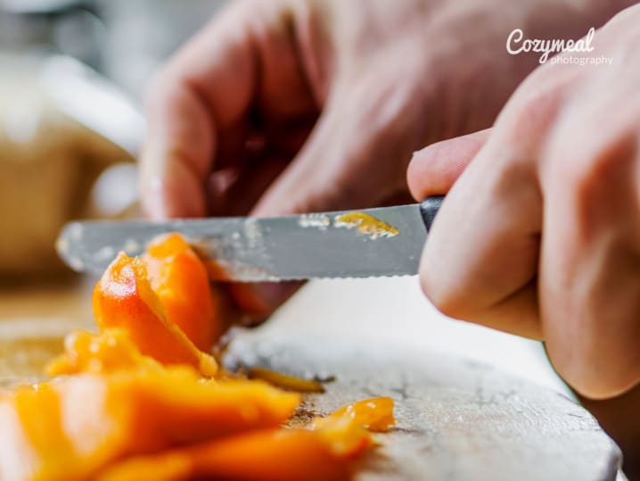 Hands slicing apricots on a wooden cutting board