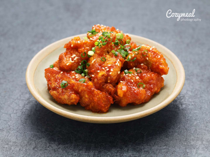 Korean fried chicken with scallions and sesame â€“ A plate of crispy glazed Korean chicken garnished with sliced scallions and sesame seeds.