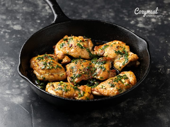 pan-roasted chicken thighs garnished with herbs in cast iron skillet