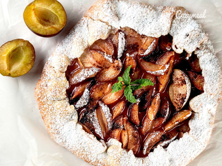Plum galette with golden crust â€“ A rustic plum galette with a golden, sugar-dusted crust, garnished with mint and surrounded by halved plums.