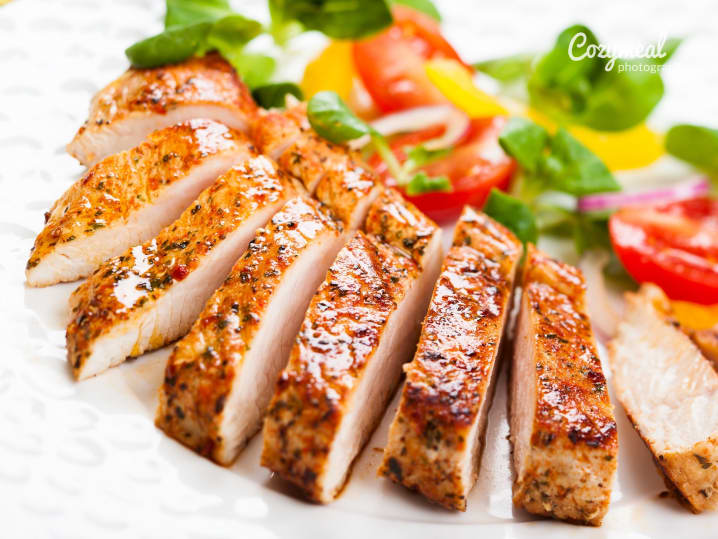 Sliced roasted chicken breast with salad â€“ Juicy, herb-seasoned chicken breast sliced and served with a fresh tomato and greens salad on a white plate.