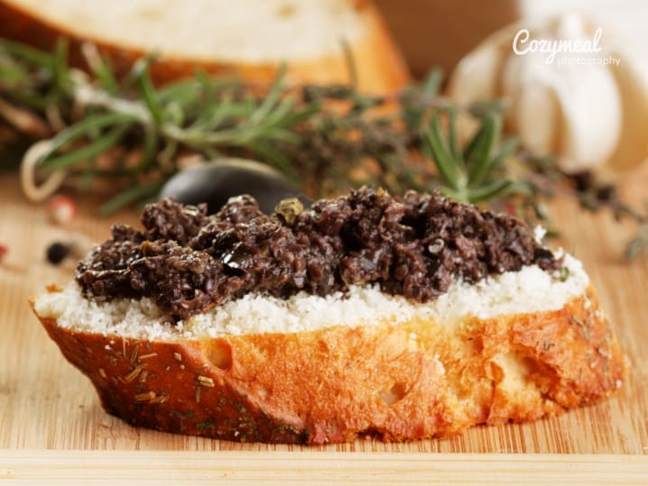 Slices of bread topped with black olive tapenade and fresh herbs
