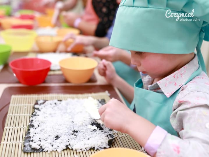 a little kid making sushi rolls in a cooking class for kids