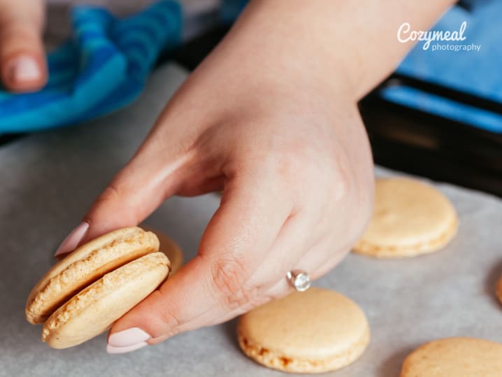 Assembling macarons with filling â€“ A close-up of hands gently pressing together two macaron shells with filling to create a complete sandwich.