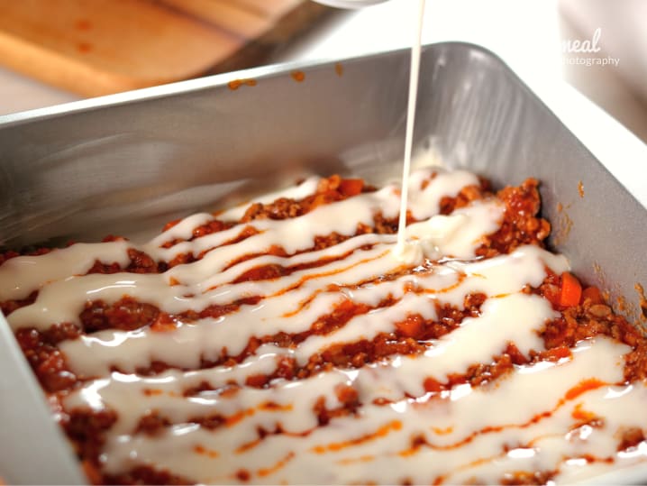 bechamel sauce being poured over lasagna bolognese