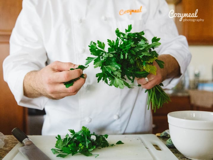 Chef holding fresh parsley in kitchen â€“ A chef in a white coat holding a bunch of fresh parsley, mid-prep in a bright kitchen.