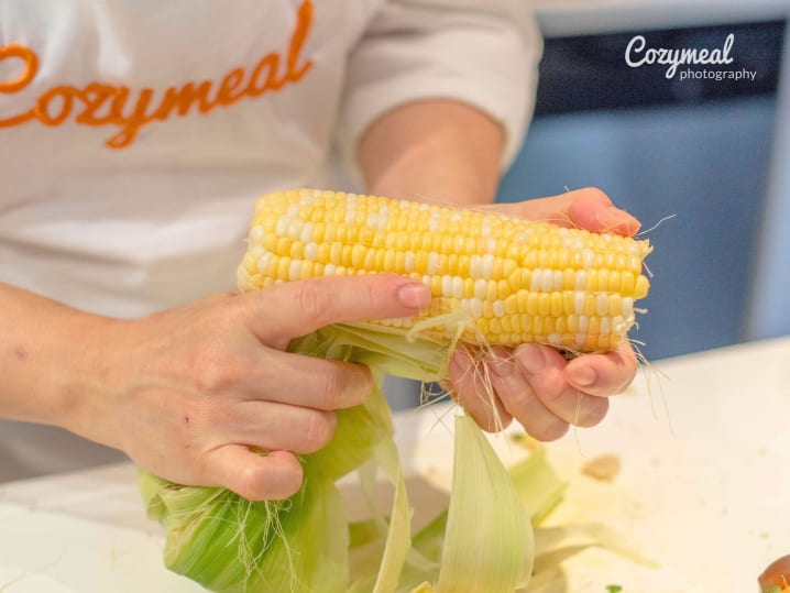 Chef in Cozymeal apron peeling corn cob