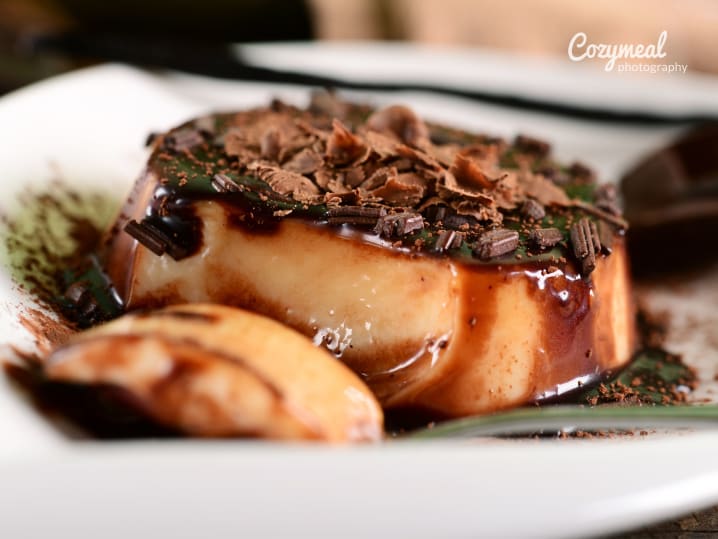 chocolate panna cotta on a white plate elegantly topped with shaved chocolate and sauce