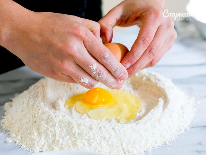 cracking an egg into flour to make homemade pasta dough