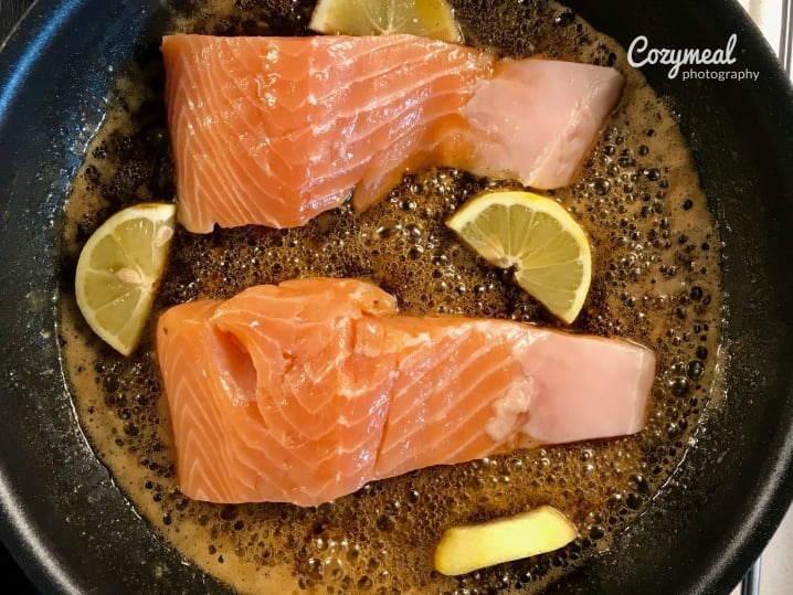 glazing salmon in a pan with lemons