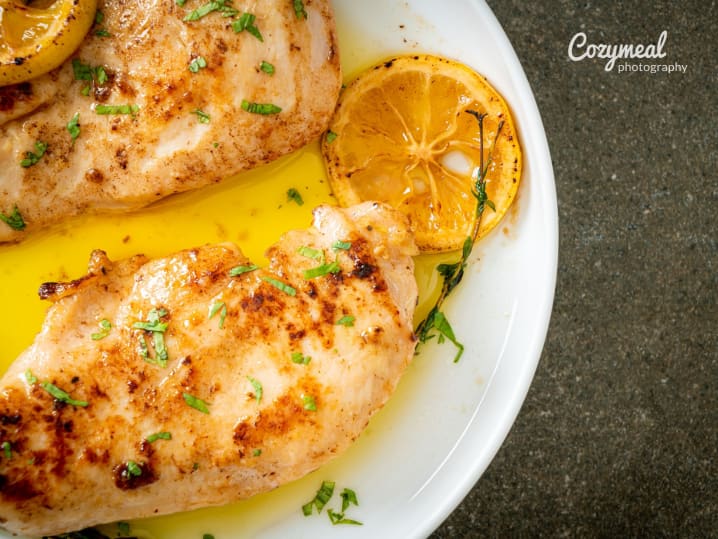 Grilled chicken with lemon and herbs â€“ Juicy grilled chicken breasts served in a lemon and herb sauce, garnished with fresh herbs and charred lemon slices.