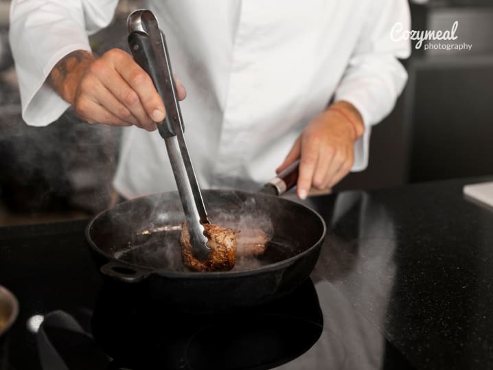 grilling steak in a plan up close using tongs for searing the sides evenly