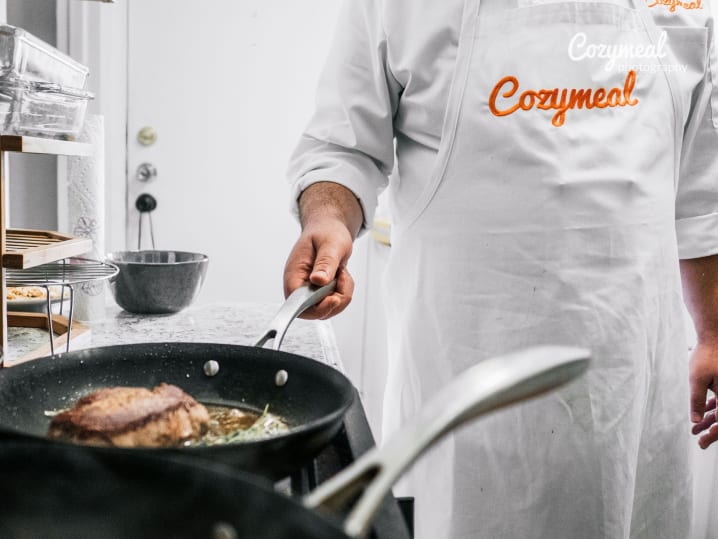 grilling steak while wearing a Cozymeal apron