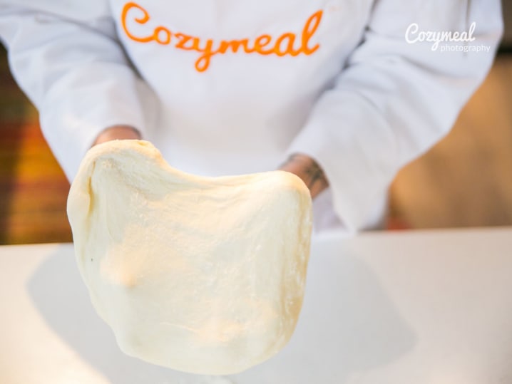 chef in Cozymeal apron kneading fresh pizza dough