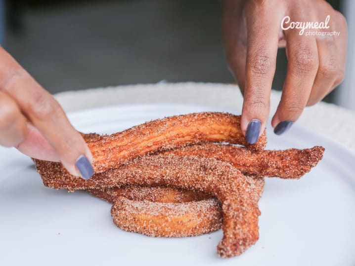 Rolling churros in cinnamon sugar â€“ Hands placing freshly fried churros onto a plate, coated in a layer of cinnamon sugar.