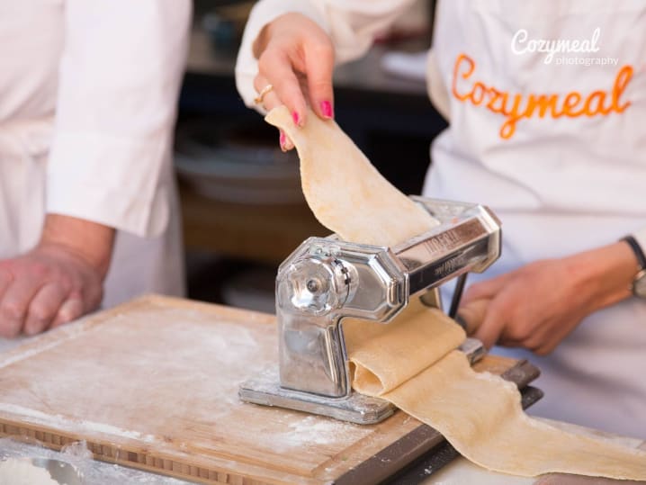 chef in Cozymeal apron making fresh pasta dough using pasta machine