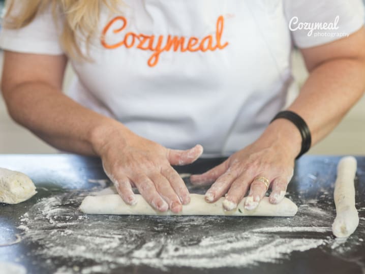 Rolling potato gnocchi dough by hand â€“ A person shaping gnocchi dough on a floured surface while wearing a â€œCozymealâ€ apron.