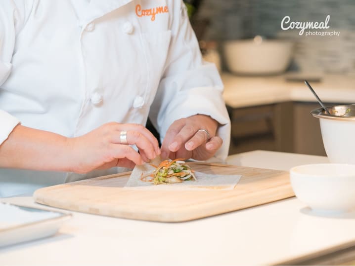 Chef assembling fresh spring rolls â€“ A chef carefully wrapping spring rolls on a wooden cutting board with fresh ingredients.