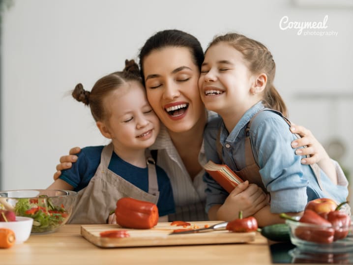 mom hugging two daughters while in kitchen aprons