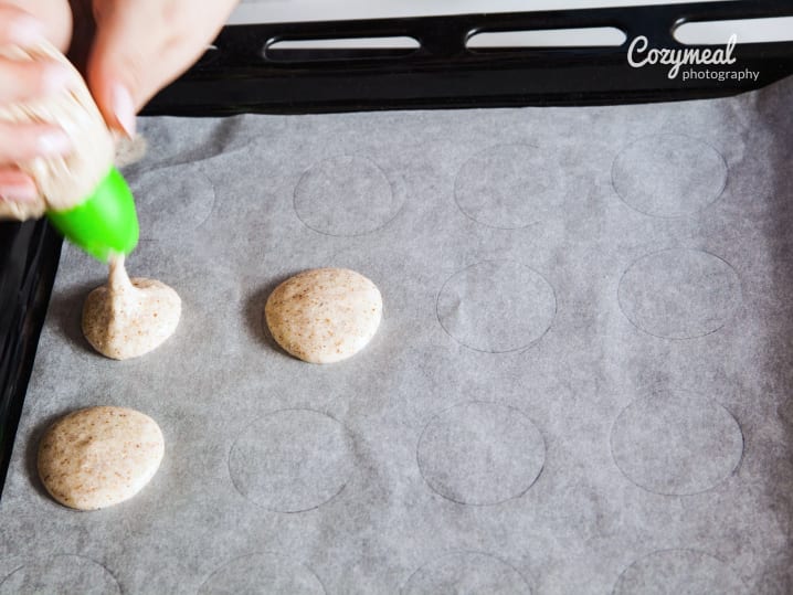 piping macaron shells onto baking sheet