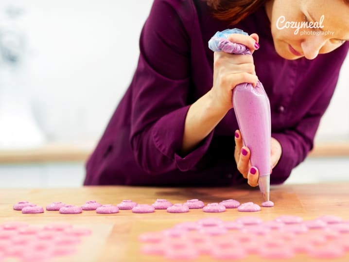 chef carefully piping blueberry macaron shells onto baking sheet