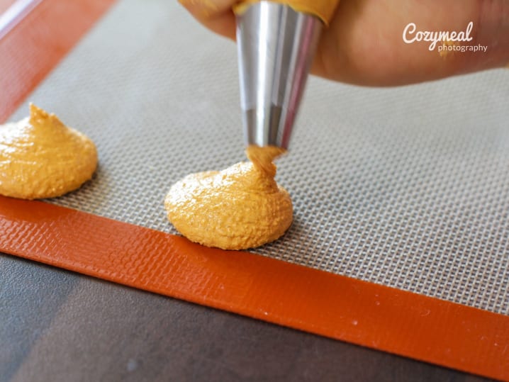 Piping macaron shells onto baking mat â€“ A hand piping neat circles of macaron batter onto a silicone baking mat.