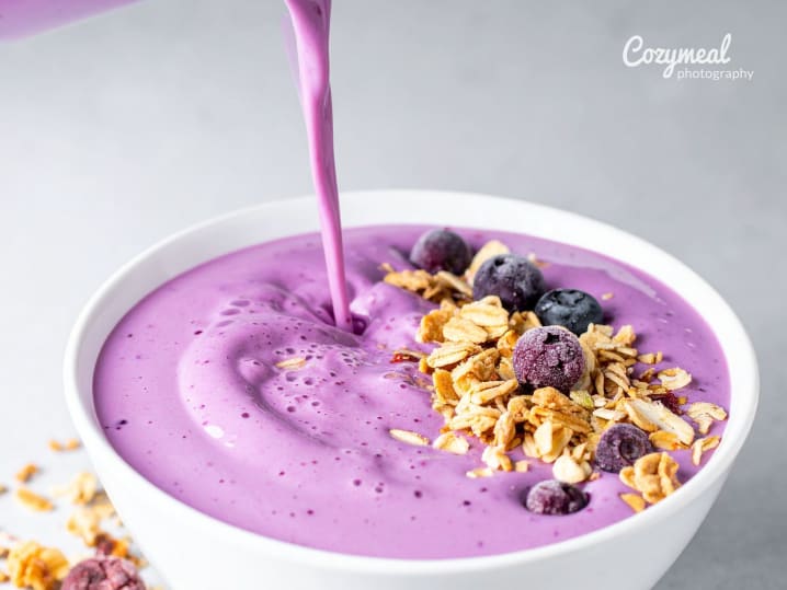 pouring smoothie over granola in a bowl