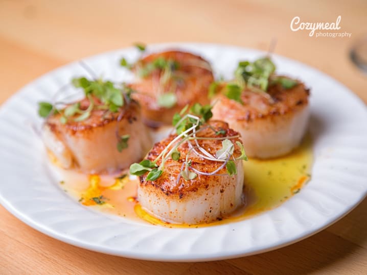 Plated scallops with microgreens â€“ Seared scallops plated with a vibrant yellow sauce and garnished with fresh microgreens, served on a white dish.