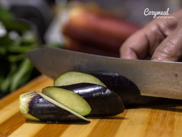 slicing eggplant on a wooden cuting board