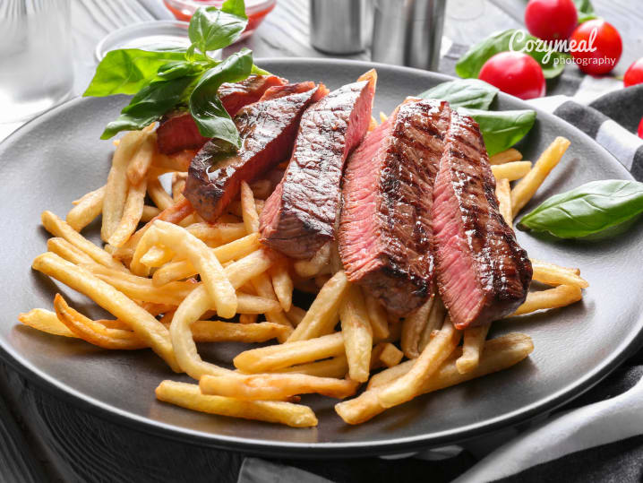 Plate of steak cooked medium-rare, served with crispy French fries and garnished with fresh basil.