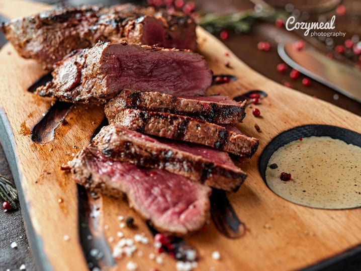 sliced medium-rare steak served on wooden cutting board with a mustard sauce
