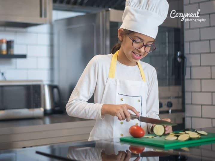 smiling teen girl in chef attire chopping vegetables in professional kitchen