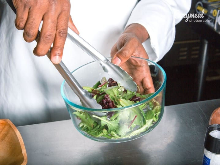 tossing salad in a glass bowl using tongs