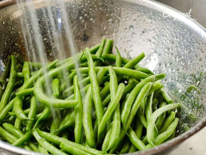Washing haricots verts in colander â€“ A batch of fresh green beans being rinsed in a metal colander under running water.