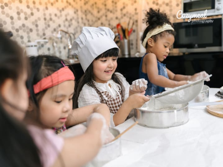 Group of kids wearing chef hats and aprons, mixing ingredients together at a table during a baking class.