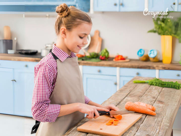 a teenage girl is chopping vegetables while wearing an apron