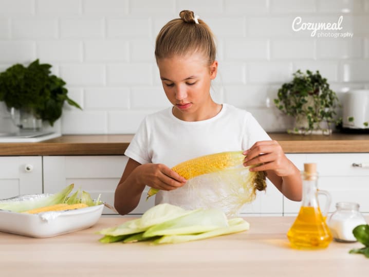 teen girl is peeling fresh corn in a kitchen