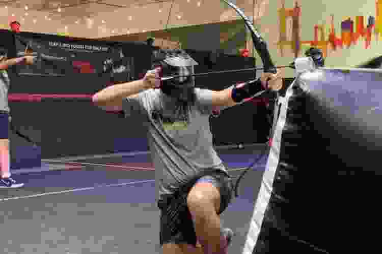 a helmeted archery player kneels down with a foam-tipped arrow pulled back 