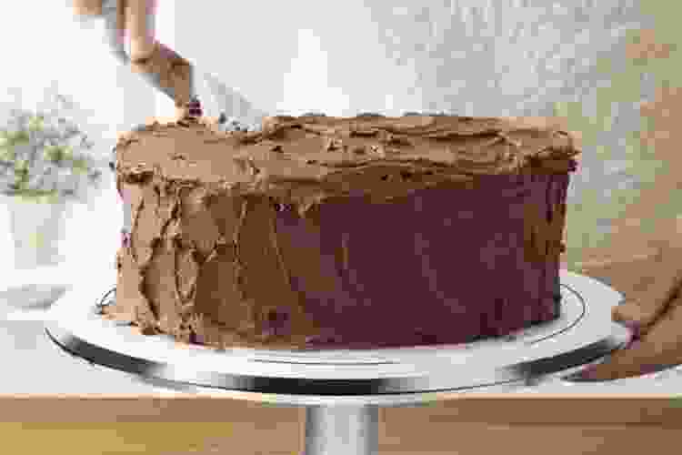 chef icing chocolate cake on a rotating cake stand