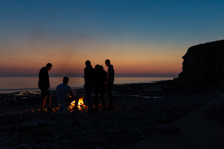 friends gathered around a beach bonfire at sunset