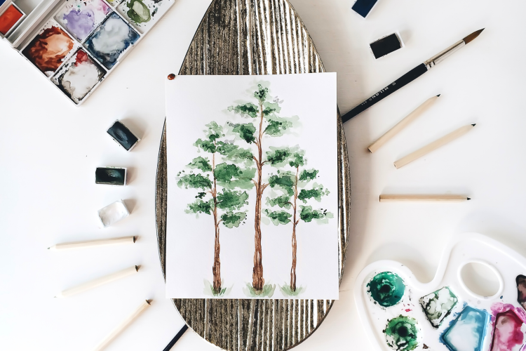 forest watercolor painting surrounded by painting supplies