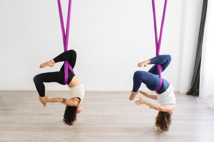 two woman upside down in aerial yoga class